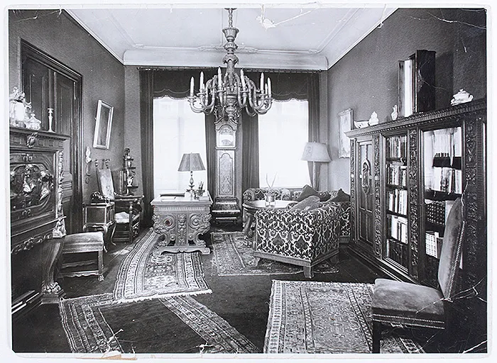Black-and-white image. View of a living room with heavy wooden furniture and several rugs.