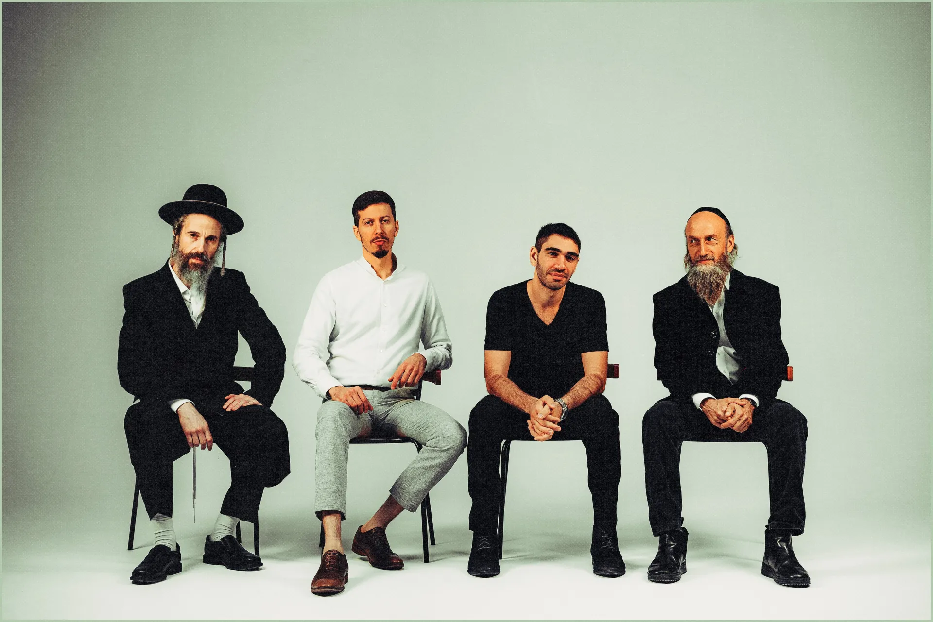 Vier M&auml;nner sitzen in einer Reihe auf St&uuml;hlen und schauen l&auml;ssig in die Kamera.