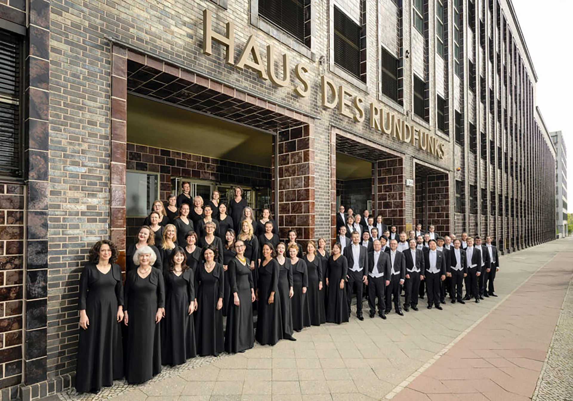 Die Mitglieder des Rundfunkchores Berlin stehen, schwarz gekleidet, vor dem Haus des Rundfunks.