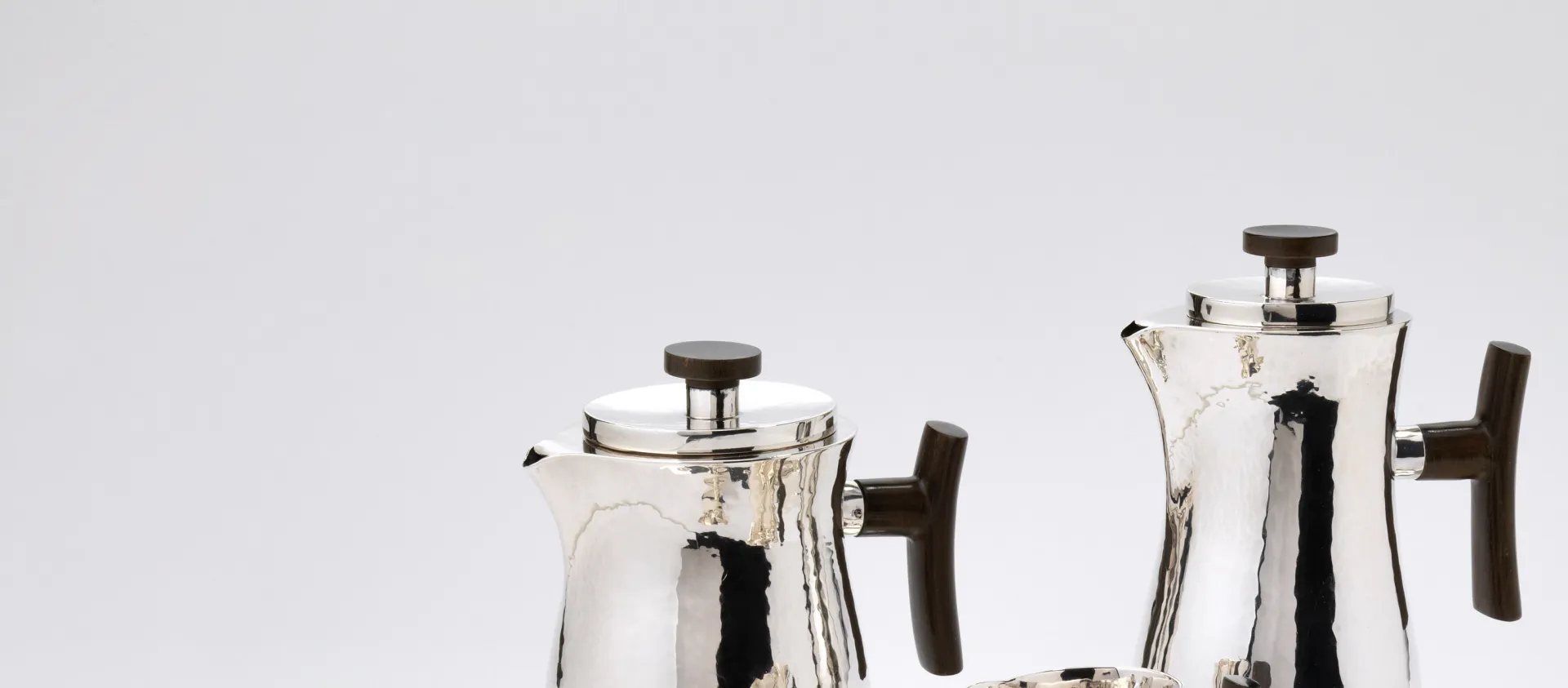 Das Bild zeigt ein Tablett mit einem Kaffee- und Teeservice, das zwei Kannen und zwei becherartige Behälter umfasst. Das Material ist Silber.