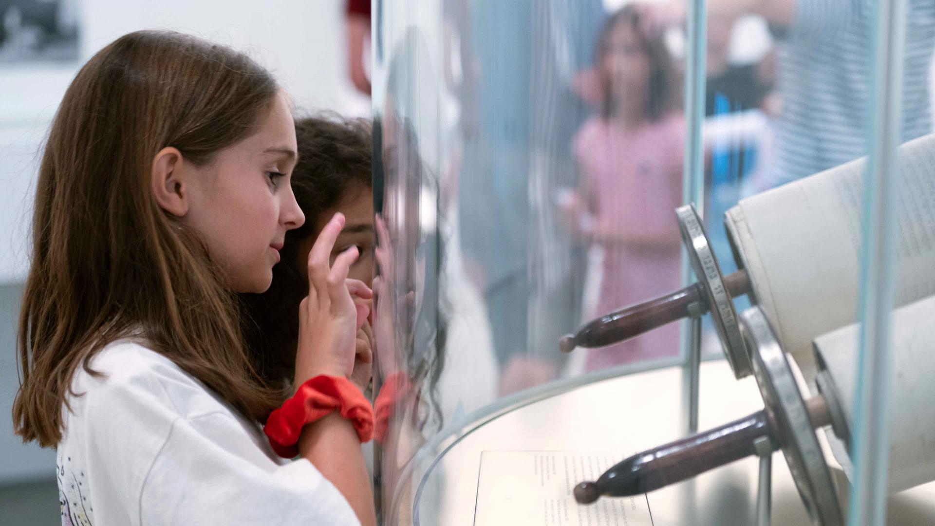 Zwei Kinder betrachten eine Tora-Rolle, die sich hinter einer gewölbten Glasscheibe befindet.