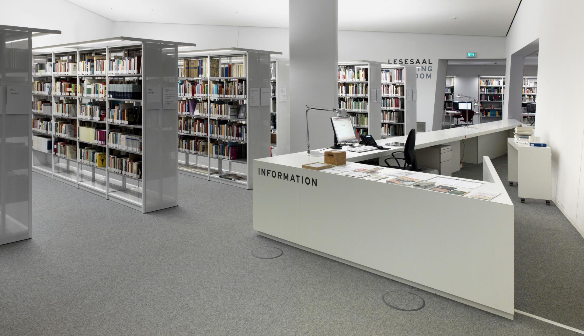 Helle Räumlichkeit, in der Innenausstattung dominiert durch spitze geometrische Formen im Stil des Libeskind Museumsgebäude mit Bücherregalen und Informationstheke