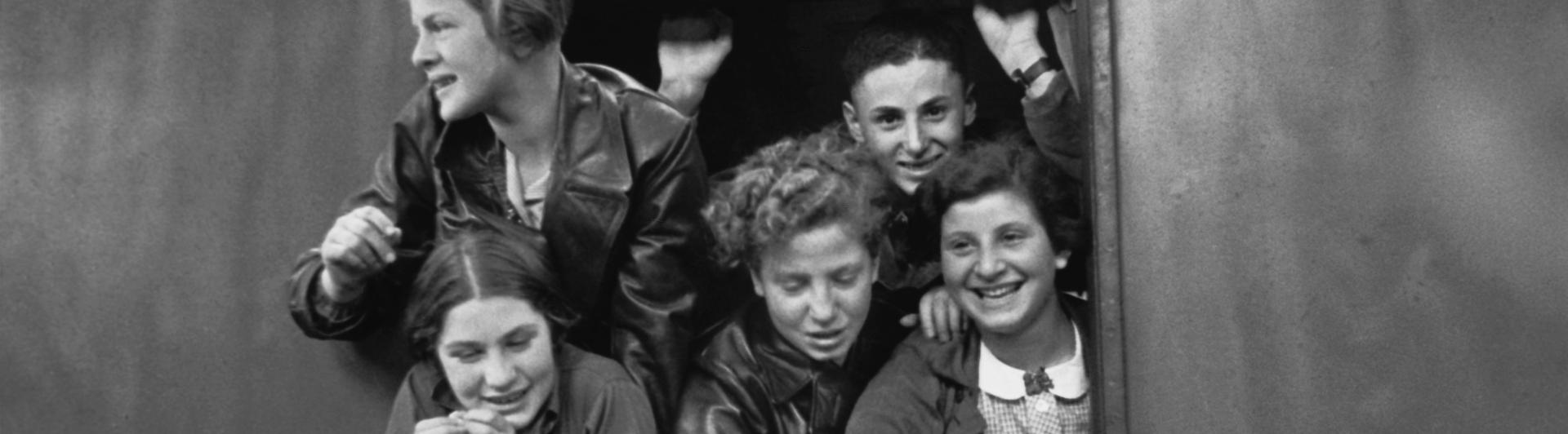 Schwarz-Weiß-Fotografie jugendlicher Jungen und Mädchen, die sich lachend aus einem Zugfenster lehnen