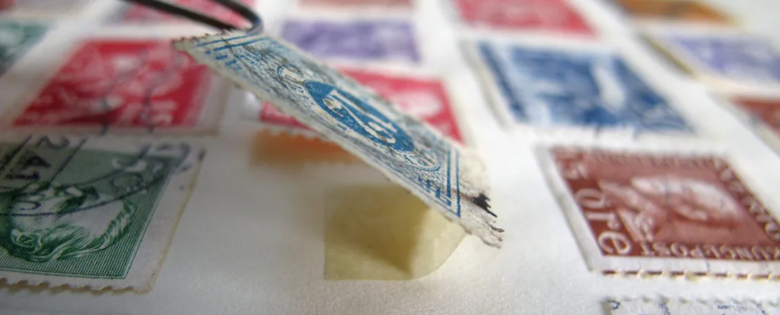 Pinzette hebt Briefmarke in einem Album an.