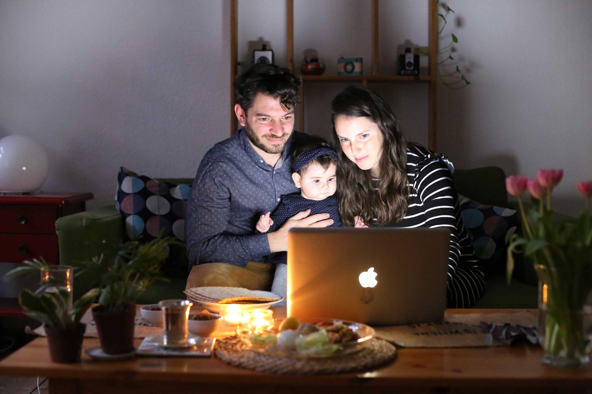 A man, a child and a woman sitting in front of a laptop