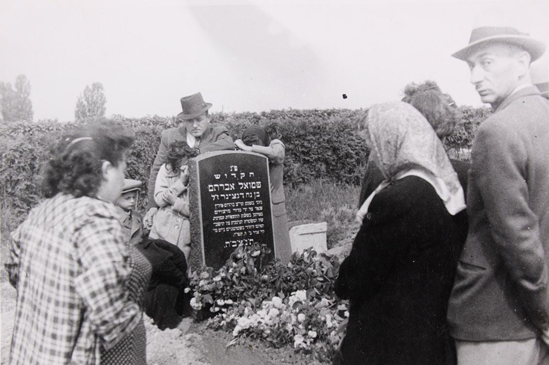 Black and white photograph of people at a grave with flowers.