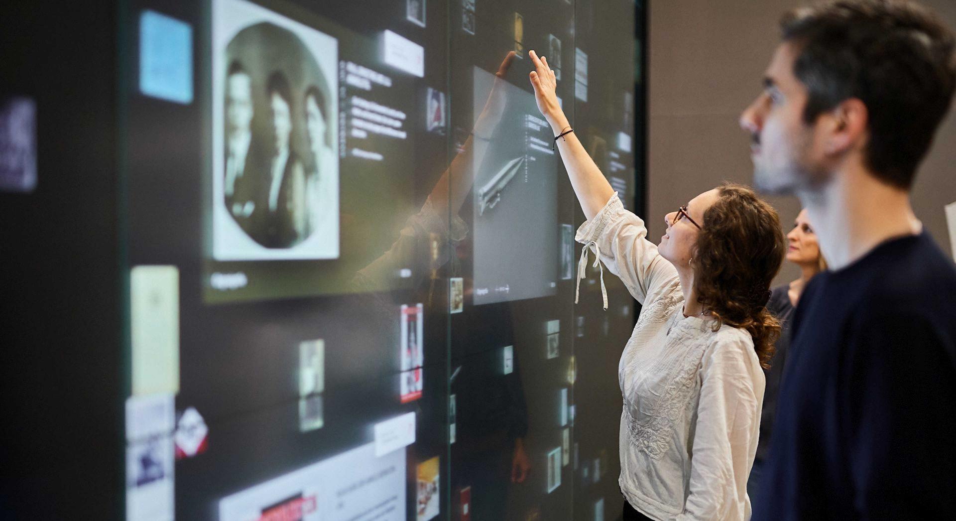 Menschen berühren eine große Touchscreen-Wand, auf der Dokumente und Objekte zu sehen sind
