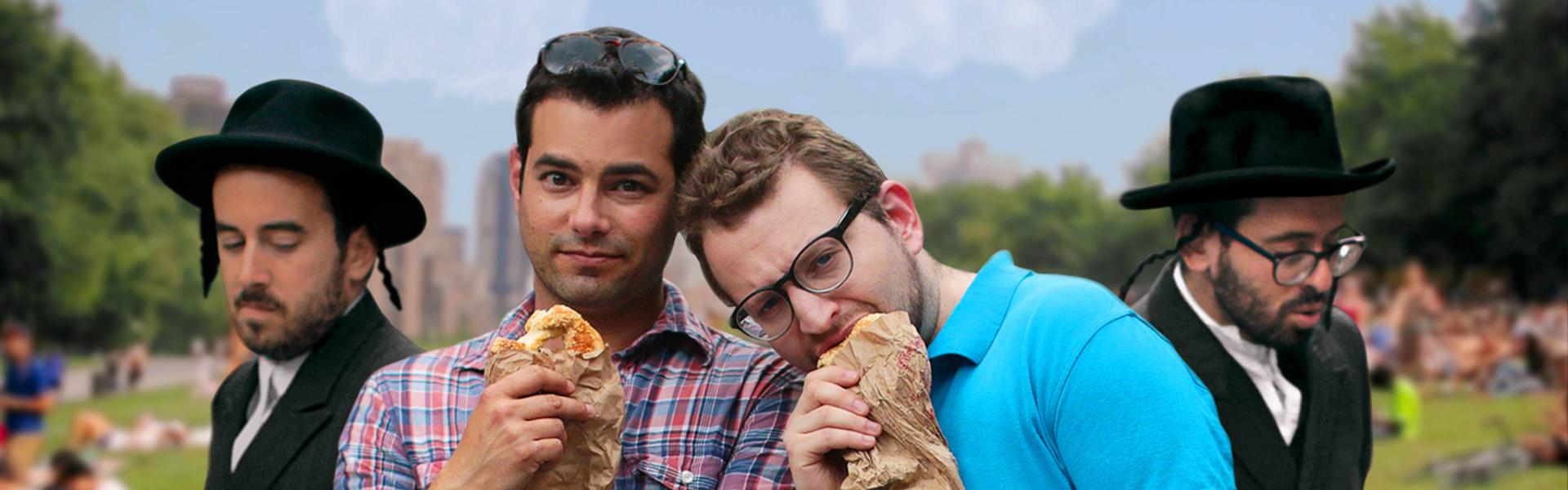 Two men in short-sleeved shirts are standing in the park, eating baked goods out of paper bags and looking at the camera; next to them are two men dressed in Jewish Orthodox clothing.