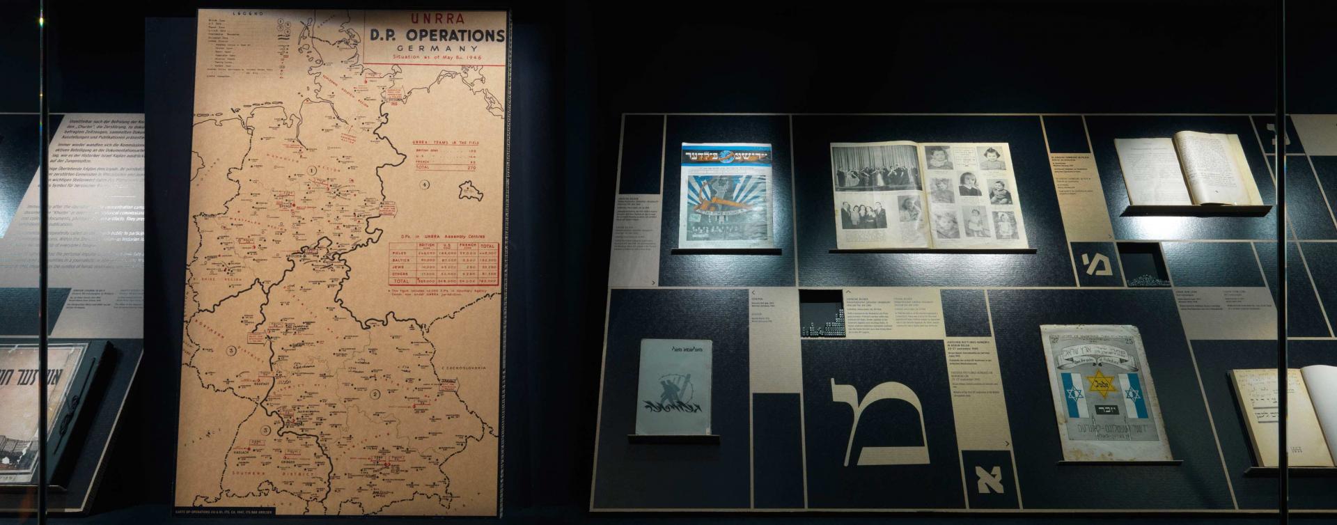 Eine Vitrine mit einer Deutschlandkarte, auf der DP-Lager verzeichnet sind, verschiedenen Publikationen und hebräischen Lettern in verschiedener Typografie