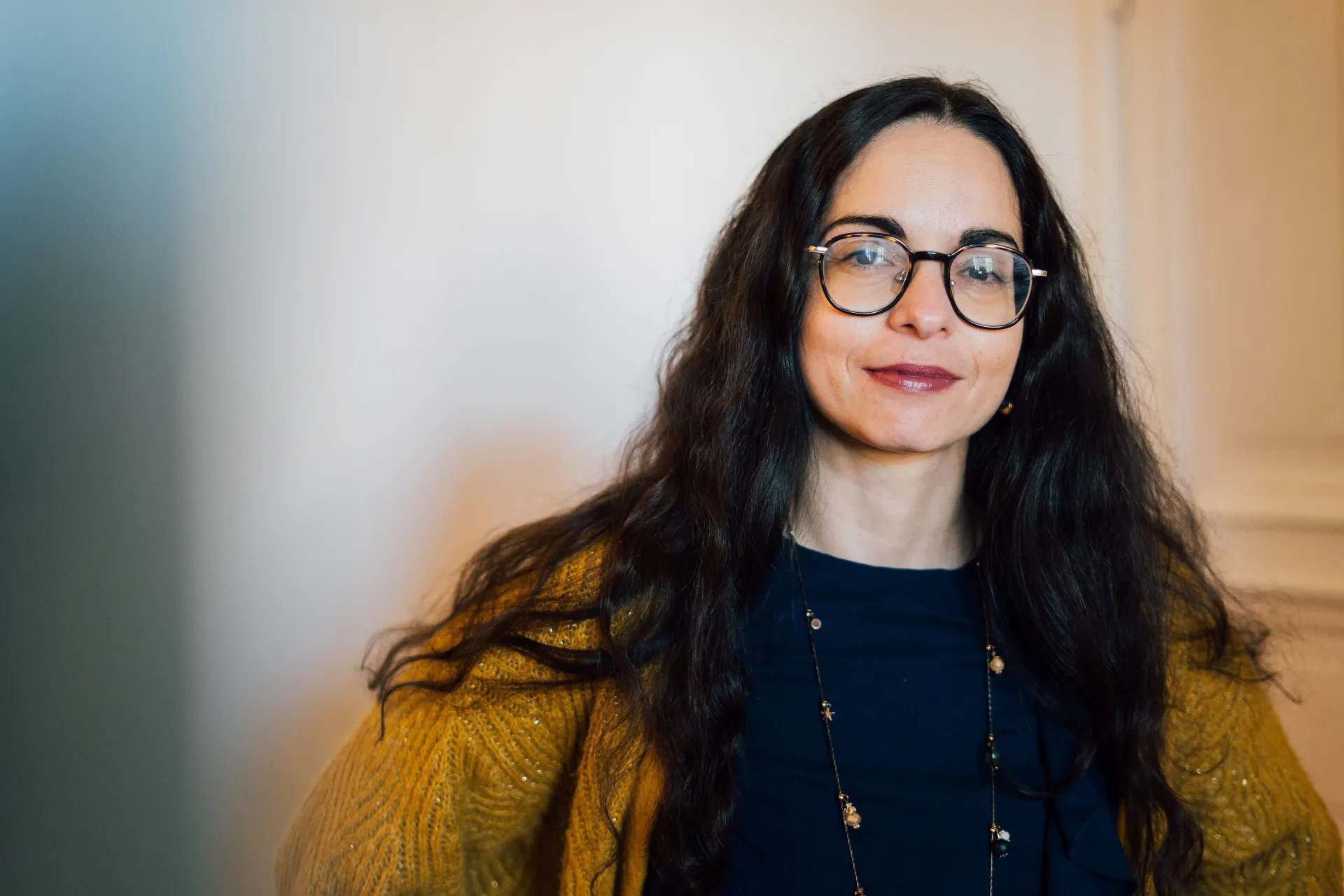 A woman with dark, long hair and glasses looks friendly into the camera.