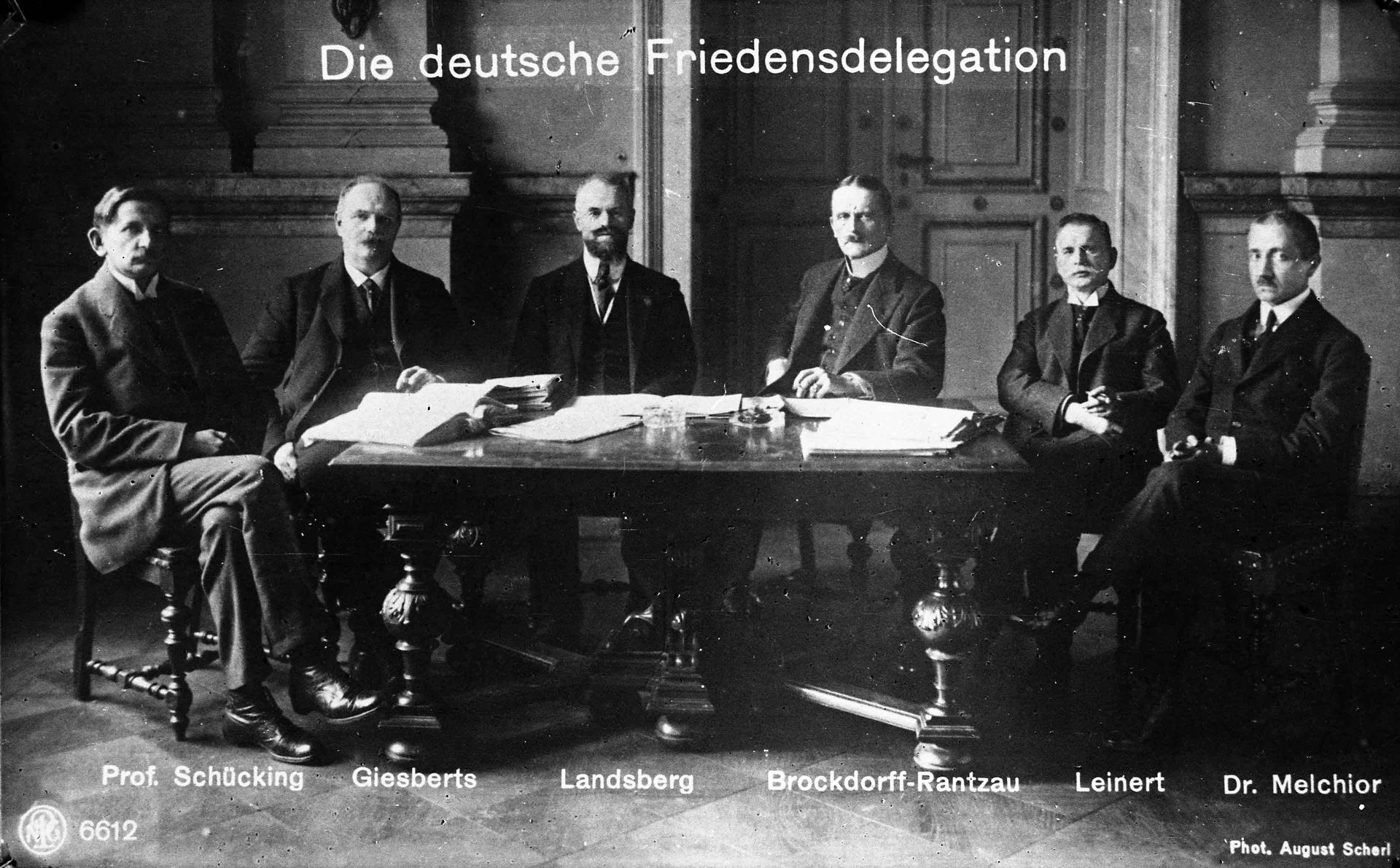 Gruppenbild der deutschen Delegation für die Friedensverhandlungen in Versailles um runden Tisch sitzend