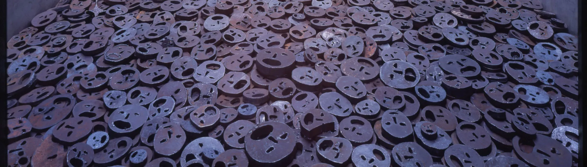 Menashe Kadishmans Installation: zahlreiche Eisenplatten, in die Gesichter geschnitten sind, liegen auf dem Boden eines Voids.