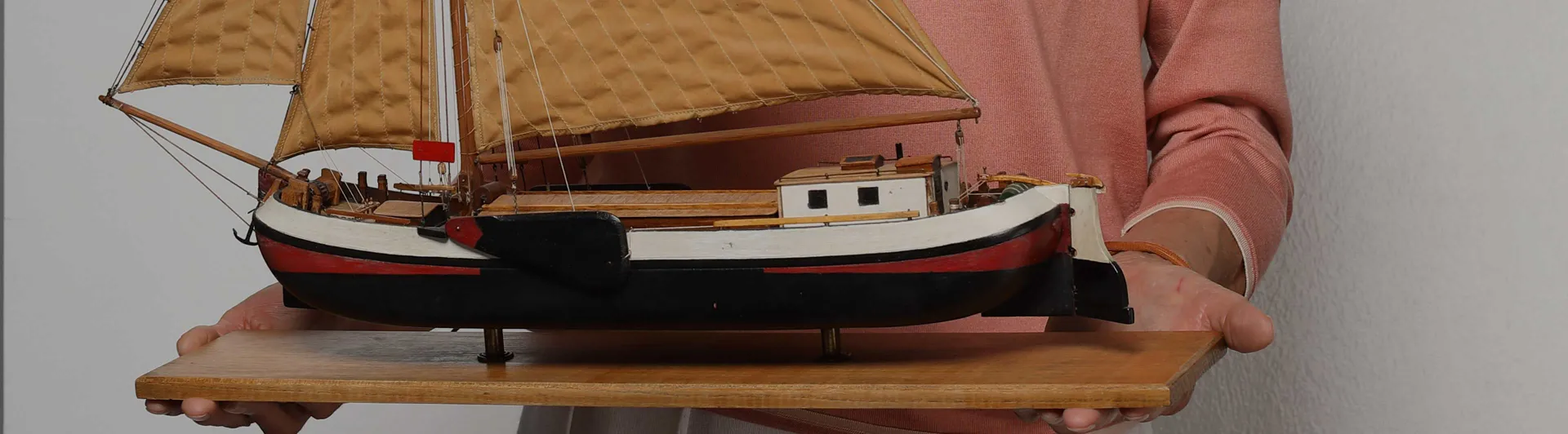 Hands holding a wooden board with a model ship on it.