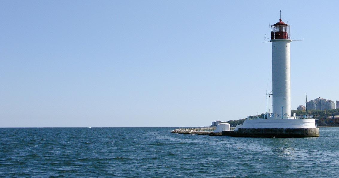 View of the sea, a lighthouse on the right, tall houses in the background.