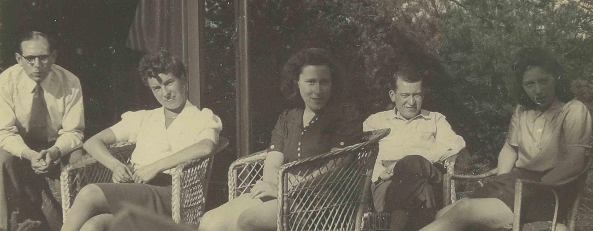 Schwarz-weiß Fotografie von zwei Männern und drei Frauen, die auf Stühlen in einem Garten sitzen.