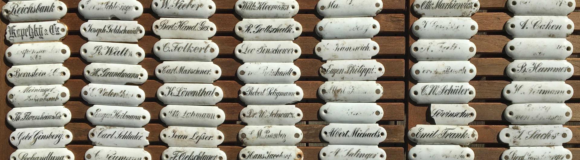 Numerous small white porcelain name tags are lined up on a wooden table. 
