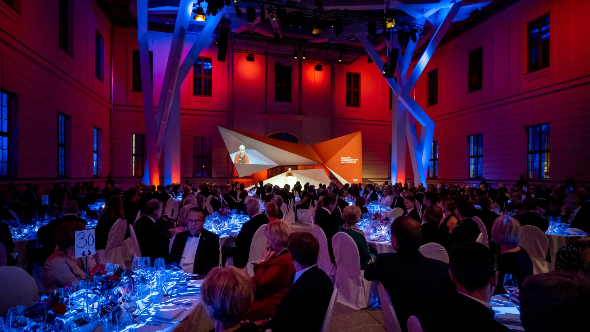 Banquet hall with guests at tables and an illuminated stage in the background.