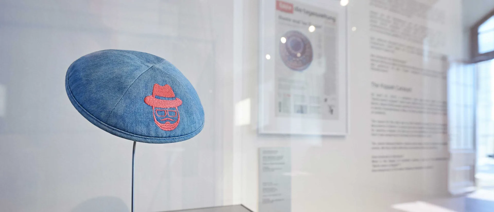 Kippa aus Jeansstoff und mit Stickerei auf einem Metallständer.
