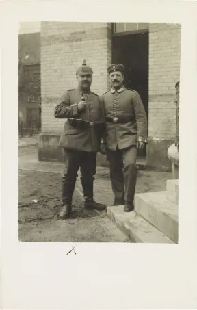 Schwarz-wei&szlig;-Foto: Zwei uniformierte Soldaten mit Pickelhaube bzw. Milit&auml;rm&uuml;tze, vor einem Geb&auml;ude stehend