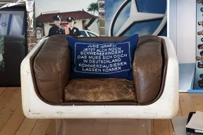 Blaues Kissen mit gleichm&auml;&szlig;igerer, wei&szlig;er Aufschrift in einem abgewetzten braunen Ledersessel