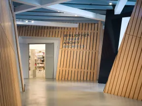 Blick in einen mit Holzpanelen verkleideten Flur, an dessen Ende sich eine ge&ouml;ffnete T&uuml;r befindet. An der Wand rechts neben der T&uuml;re steht "Bibliothek, Archiv