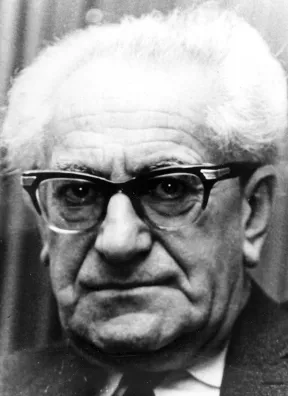 Black-and-white portrait of a white-haired man with glasses looking sternly into the camera.