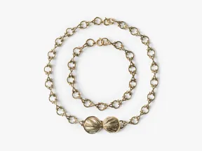 Das Bild zeigt eine Kette und ein Armband, die aus goldenen, runden Gliedern zusammengesetzt sind. 