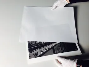 two hands with white gloves hold the photo The Elevated and Me by Ilse Bing in the envelope