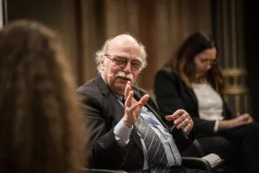 Ein &auml;lterer Mann sitzt in einer Gespr&auml;chsrunde. Er spricht die Gespr&auml;chspartnerin, schaut ein wenig nach links und hebt beim Sprechen eine Hand.  