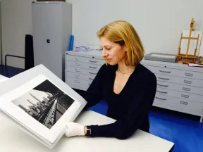 A woman with blonde hair and a dark top holds the photo of Ilse Bing in her hands