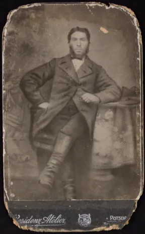 Black and white image. A man is sitting leaning against a table. 