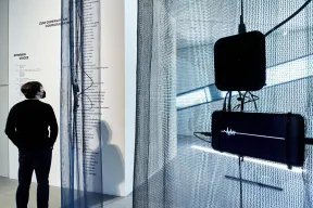 Raumansicht der Ausstellung mit Besucher, im Vordergrund ein Bildschirm mit einer Stimmwelle