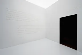 Raum mit wei&szlig;er Schrift auf wei&szlig;en W&auml;nden, rechter Hand eine schwarze T&uuml;r