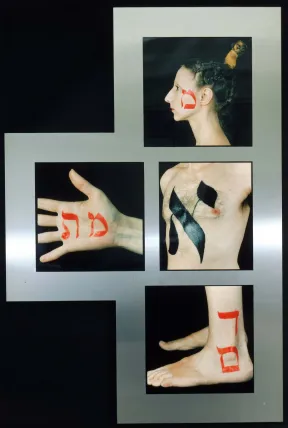 Auf einer Metalltafel sind vier Fotos von K&ouml;rperteilen montiert, die je mit 1 hebr&auml;ischen Buchstaben bemalt sind: ein Frauenkopf, eine M&auml;nnertorso, eine Hand, ein Paar F&uuml;&szlig;e.