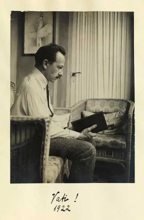 Schwarz-wei&szlig;es Foto eines Mannes im Profil, mit einem Buch in der Hand, auf einem Sofa sitzend.