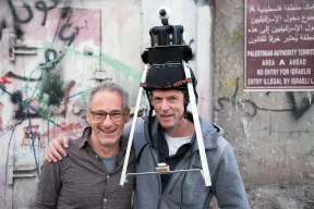 Dani Levy und Filip Zumbrunn umarmen sich, Zumbrunn tr&auml;gt eine Kamera mit Stativ auf dem Kopf