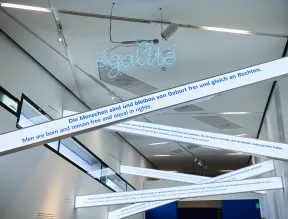 Schriftzug &eacute;galit&eacute; in Neonleuchtschrift, darunter schr&auml;g durch den Raum h&auml;ngende Zitate wie: Die Menschen sind und bleiben von Geburt frei und gleich an Rechten.