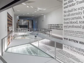 L&auml;nglicher Ausstellungsraum, an der rechten Wand ist Schrift in gro&szlig;en Lettern zu sehen, in den Boden ist eine Vitrine eingelassen