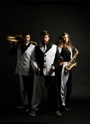 Trio in schwarz-wei&szlig;en Anz&uuml;gen vor schwarzem Hintergrund, der Mann und die Frau an den R&auml;ndern halten Saxophone