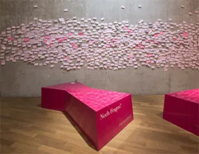 Eine Wand mit pinken Post-its beklebt, davor zwei liegende Vitrinen mit der Aufschrift &raquo;Noch Fragen?&laquo;