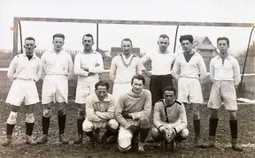 Schwarz-Wei&szlig;-Foto einer Fu&szlig;ballmannschaft vor einem Tor, in hellen Trikots und Hosen.