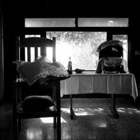 Schwarz-wei&szlig; Fotografie zeigt einen Tisch vor einem Fenster mit einer Babyschale, links davon ein Stuhl