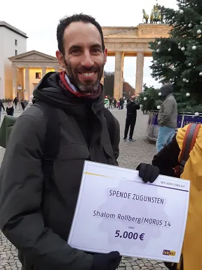 Mann h&auml;lt l&auml;chelnd Scheck &uuml;ber 5000 &euro; in die Kamera