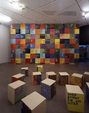 In front of a wall with labeled colored squares lie labeled color cubes