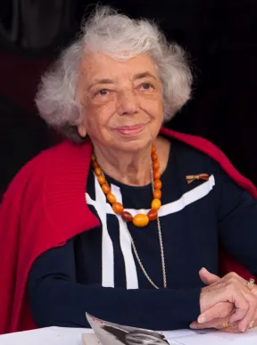 Woman (Margot Friedl&auml;nder) with white hair and striking amber necklace looks friendly into the camera.