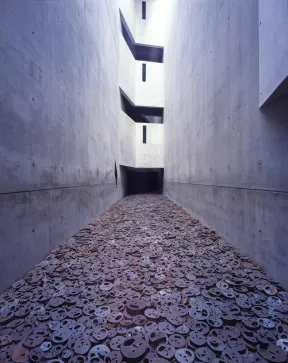 Menashe Kadishmans Installation: zahlreiche Eisenplatten, in die Gesichter geschnitten sind, liegen auf dem Boden eines Voids.