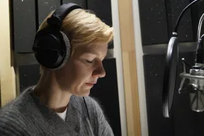 The actress and speaker Sandra H&uuml;ller sits with headphones in front of the microphone in the recording studio