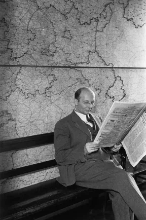 Schwarz-Wei&szlig;-Fotografie: Ein sitzender Mann liest Ausgabe der C.V.-Zeitung. Hinter ihm an der Wand ist eine Landkarte.