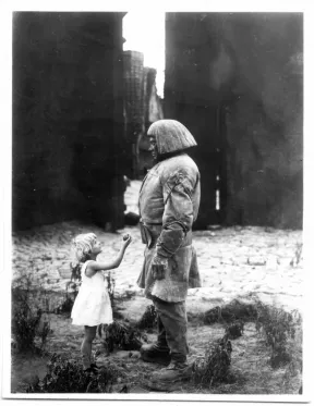 Filmstill aus dem Film &bdquo;Der Golem, wie er in die Welt kam&ldquo;: ein kleines M&auml;dchen steht vor dem Golem und reicht ihm einen Apfel.