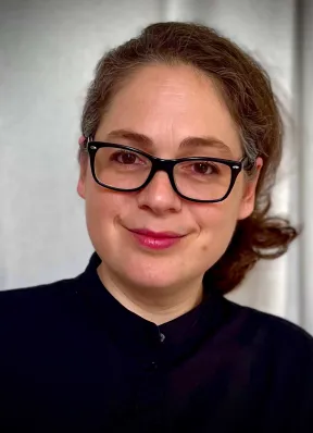 A brunette woman with dark glasses and a black sweater smiles at the camera.